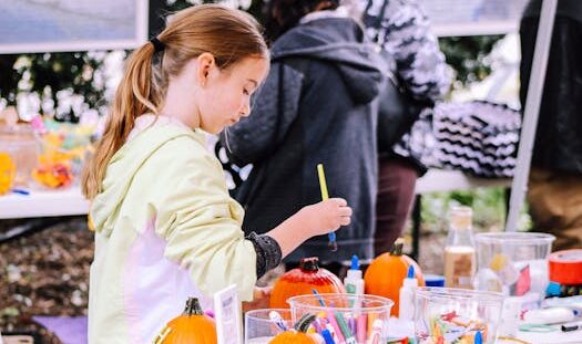 A child enjoys painting pumpkins at an outdoor crafting event, surrounded by art supplies.